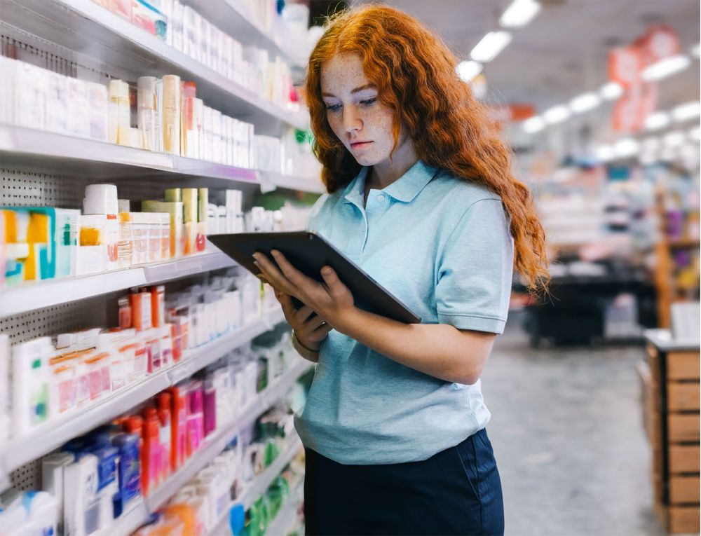 Einzelhandelsmitarbeiterin prüft Regalinhalte mit Tablet zur digitalen Unterstützung durch iNFOHUB im Drogeriemarkt