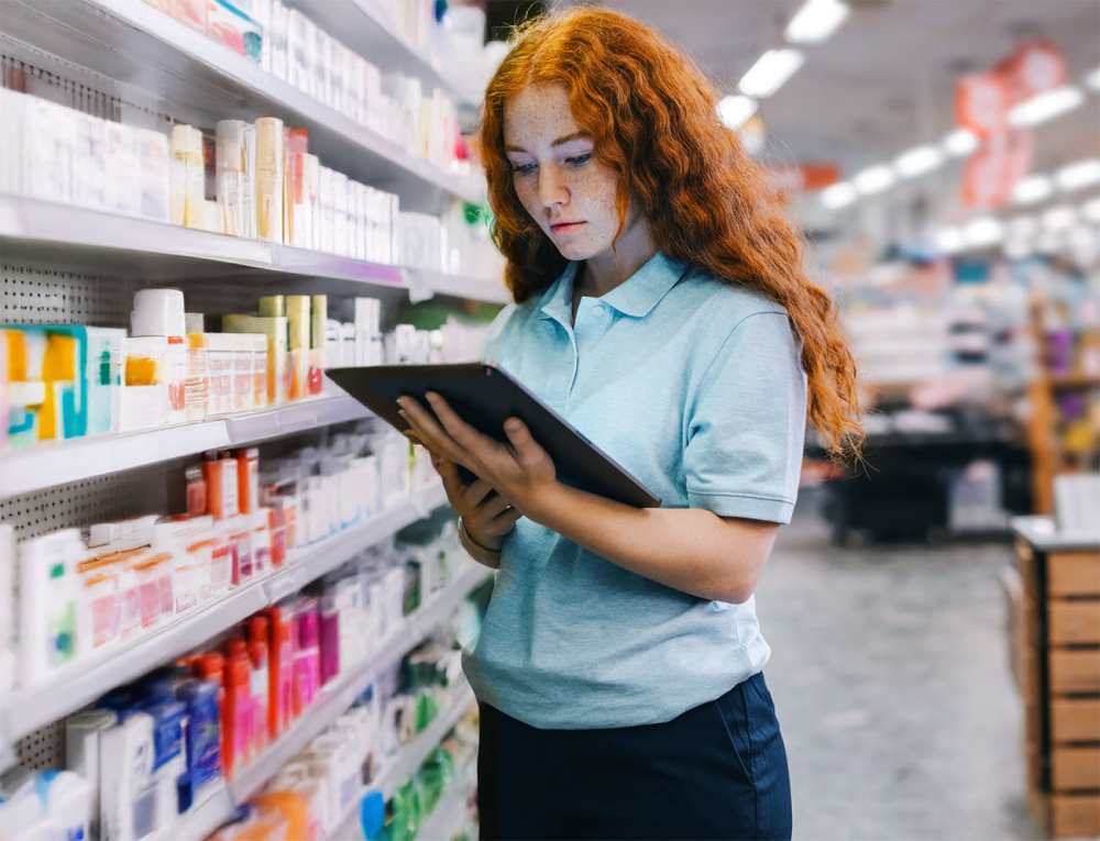 Einzelhandelsmitarbeiterin prüft Regalinhalte mit Tablet zur digitalen Unterstützung durch iNFOHUB im Drogeriemarkt